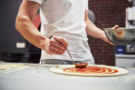 Close up view of baker putting sauce to make delicious pizza for an order in restaurant.の写真素材