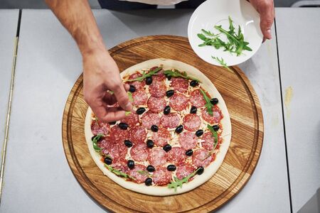 Seasonings and cheese. Top view of baker in white shirt putting olives to make delicious pizza for an order in restaurant.の写真素材