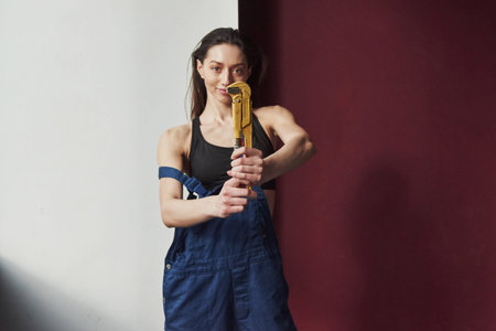 Holding yellow pipe wrench. Young housewife decided to glue wallpaper in her new house in the room.