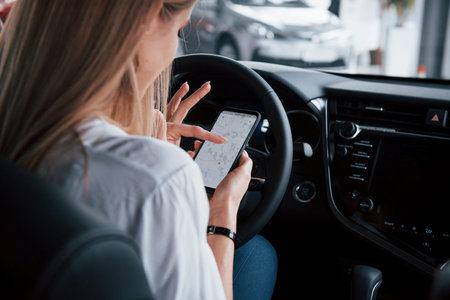 Searching for the optimal route. Beautiful blonde girl sitting in the new car with modern black...