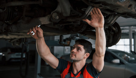 On elongated hands. Man at the workshop in uniform fixes broken parts of the modern car.