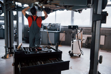 Focused on the table with different instruments. Man at the workshop in uniform fixes broken parts...