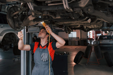 Ready for replacement. Man at the workshop in uniform fixes broken parts of the modern car.