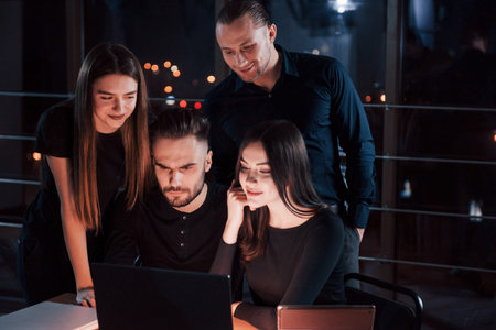 Only man with beard is serious. Team of young business people works on their project at night time...