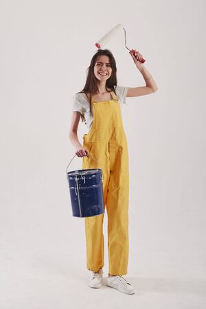 Blue bucket in hand. Brunette woman in yellow uniform stands against white background in the studio.の写真素材
