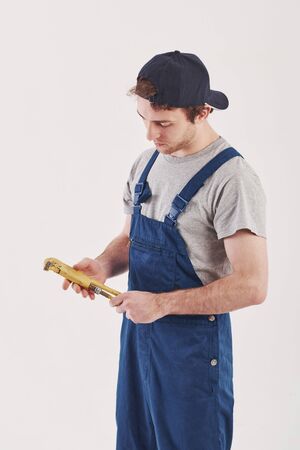 Yellow colored wrench in hands. Man in blue uniform stands against white background in the studio.の写真素材