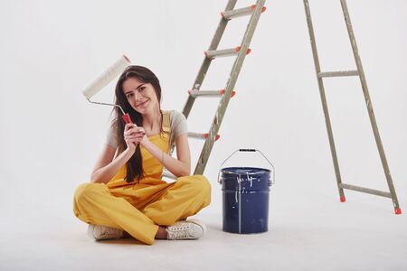 Job well done. Beautiful brunette in yellow uniform and blue colored bucket sits near the ladder.の写真素材