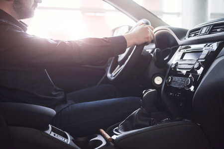 Gorgeous sunlight. Close up side view of man sitting in the modern car with black interior.