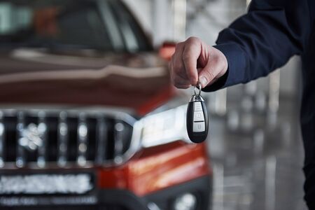 Close up view of mans hand holds keys from brand new red car that stands at background.の写真素材