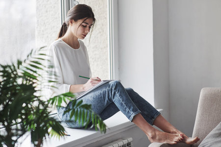 Side view. Young brunette in the room with white walls and daylight that comes from the window.