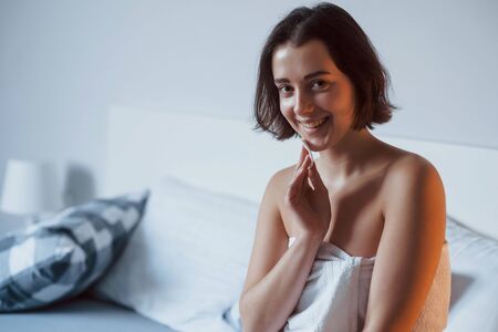Smiling for the camera. Time for a make up. Woman sits on the bed and use cosmetics to clean her skin.の写真素材
