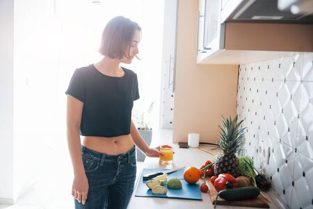 Standing in daylight that comes from the window. Girl in the modern kitchen at home at her weekend in the morning time.の写真素材