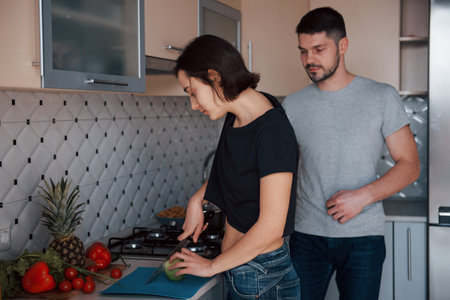 Using knife to slice the apple. Young couple in the modern kitchen at home at their weekend time in...