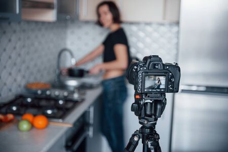 Professional camera on tripod. Girl in the modern kitchen at home at her weekend time in the morning.の写真素材