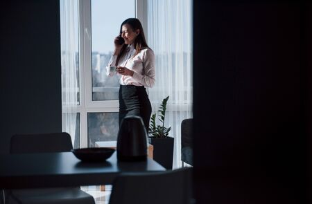 Looking through the window. Young businesswoman with black hair in official clothes at her home.の写真素材