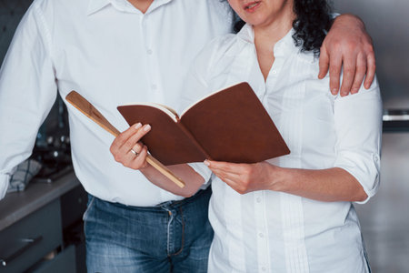 Close up view of a book. Man and his wife in white shirt preparing food on the kitchen using vegetables.の写真素材