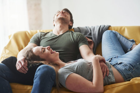 Nice joke. Happy couple relaxing on the yellow sofa in the living room of their new house.