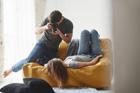 Professional equipment. Photographer taking a shot of young girl that lying on the white sofa.の写真素材