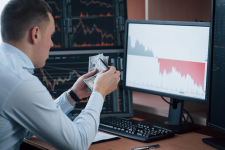 Enough money for today. Man working online in the office with multiple computer screens in index...