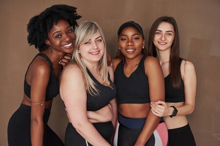 Friendship between different people. Group of multi ethnic women standing in the studio against brown background.の写真素材