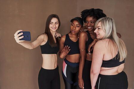Lets take a picture. Group of multi ethnic women standing in the studio against brown background.の写真素材