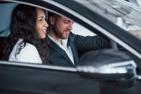 Side view. Lovely successful couple trying new car in the automobile salon.