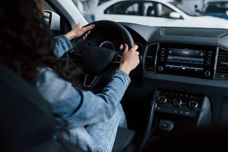 Different buttons and knobs. Cute girl with black hair trying her brand new expensive car in the automobile salon.の写真素材