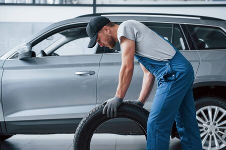 This one must fit perfectly. Mechanic holding a tire at the repair garage. Replacement of winter and summer tires.の写真素材