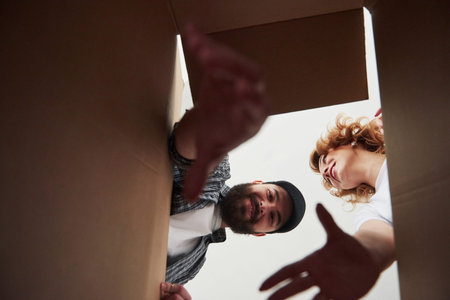 Bearded man trying to reach the item down of a box. Happy couple together in their new house....