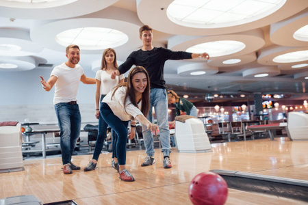 Come on, you can do it. Young cheerful friends have fun in bowling club at their weekends.