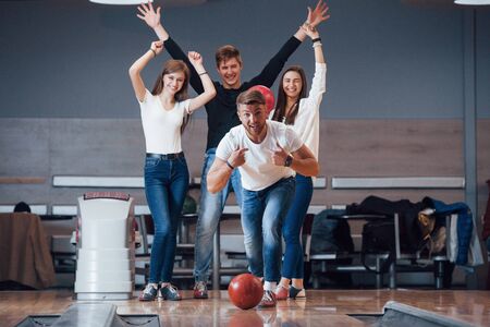 This is win. Young cheerful friends have fun in bowling club at their weekends.の写真素材