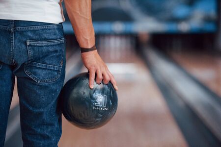 Focused photo. Rear particle view of man in casual clothes playing bowling in the club.の写真素材