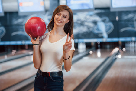 Cheerful young woman in casual clothes holding red bowling ball in the club.の写真素材