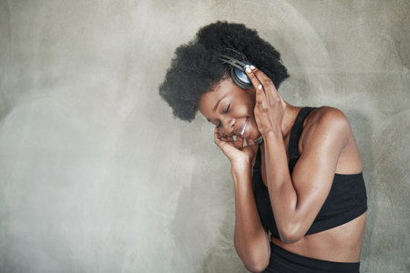 Pretty woman in headphones. Portrait of african american girl in fitness clothes having a break...