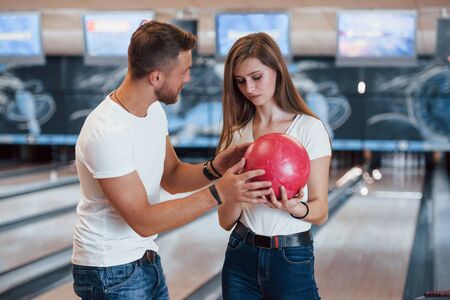 Man teaching girl how to holds ball and play bowling in the club.の写真素材