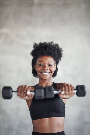 Studio shot of young woman that stands in front of grey background with dumbbells in hands.の写真素材
