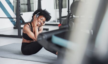 Between equipment. African american woman with curly hair and in sportive clothes have fitness day in the gym.の写真素材