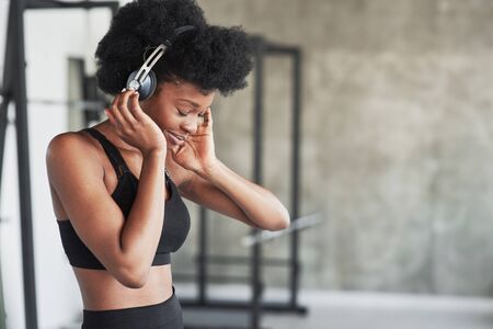 Gorgeous girl testing new headphones. African american woman with curly hair and in sportive clothes have fitness day in the gym.の写真素材