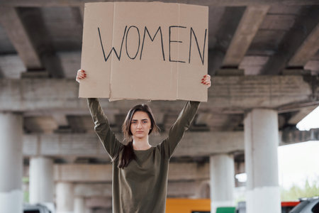 Standing alone. Pretty girl in casual clothes with handmade feminist poster in hands.の写真素材