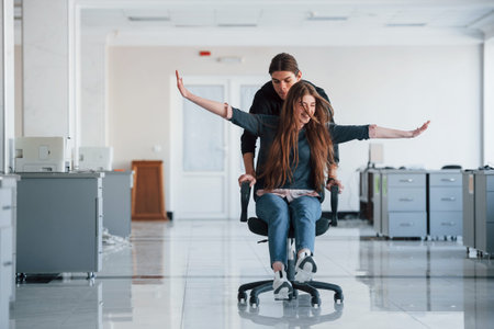 With hands to the sides. Having fun in the office. Young people have a break and driving by using a...