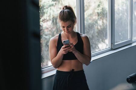 Chatting by using smartphone. Photo of gorgeous blonde woman in the gym at her weekend time.の写真素材