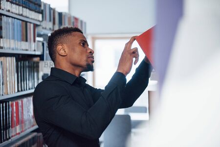 Picking red book. African american man in the library searching for some information.の写真素材