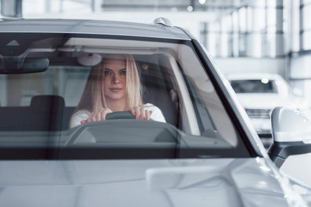 Confident look. Girl in modern car in the salon. At daytime indoors. Buying new vehicle.
