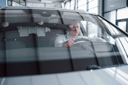 Renting automobile. Man trying new car in the salon at daytime. Buying new vehicle.の写真素材