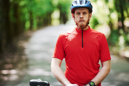 Ready and prepared. Cyclist on a bike is on the asphalt road in the forest at sunny day.の写真素材