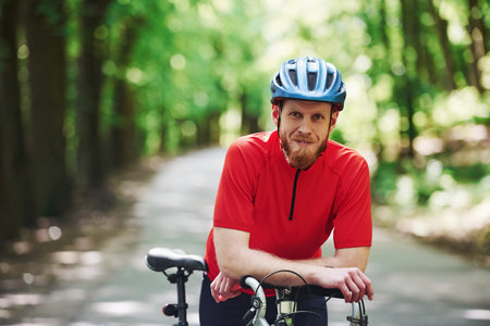 Smiling and relaxing. Cyclist on a bike is on the asphalt road in the forest at sunny day.の写真素材