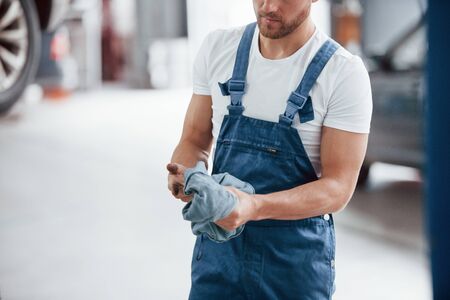 Wipes hands from oil. Employee in the blue colored uniform works in the automobile salon.の写真素材