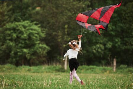 Rear view. Happy girl in casual clothes running with kite in the field. Beautiful nature.の写真素材