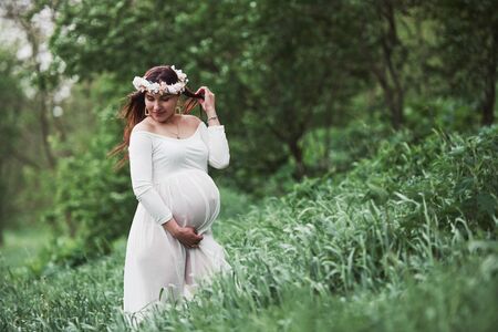 Sensuality and care. Beautiful pregnant woman in dress have a walk outdoors. Positive brunette.の写真素材