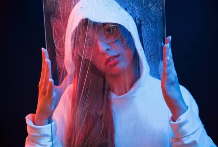 Holding wet clear material. Studio shot in dark studio with neon light. Portrait of young girl.の写真素材